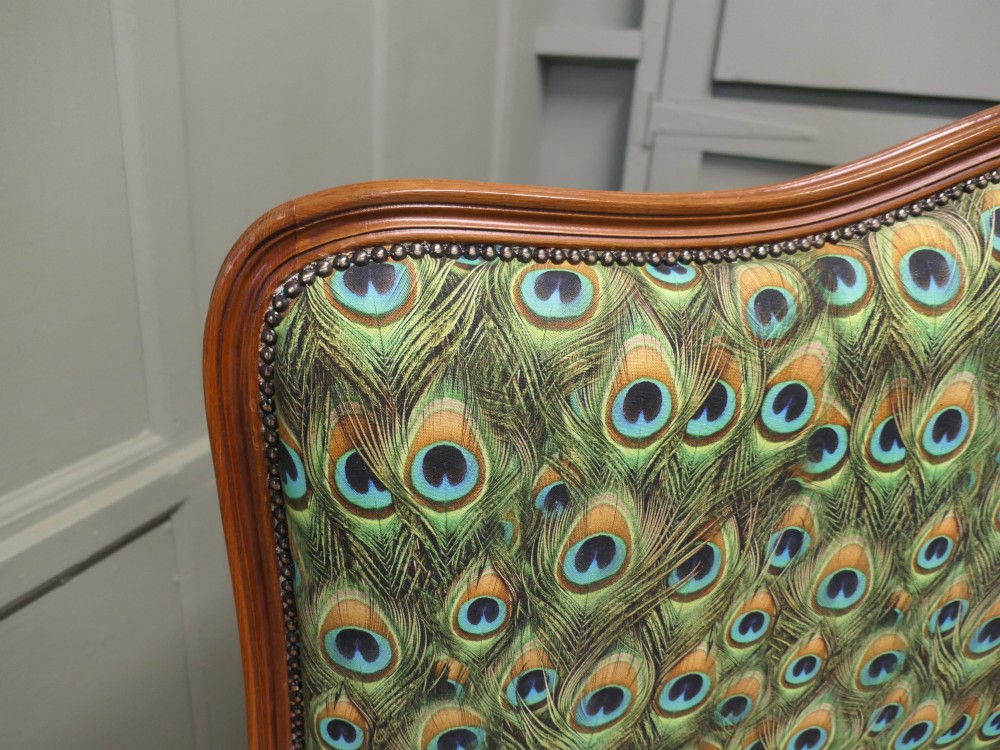 A French Louis XV style double bed frame featuring carved wooden borders, a padded headboard, and a curved corbeille footboard upholstered in green peacock feather patterned fabric with studding. View IV