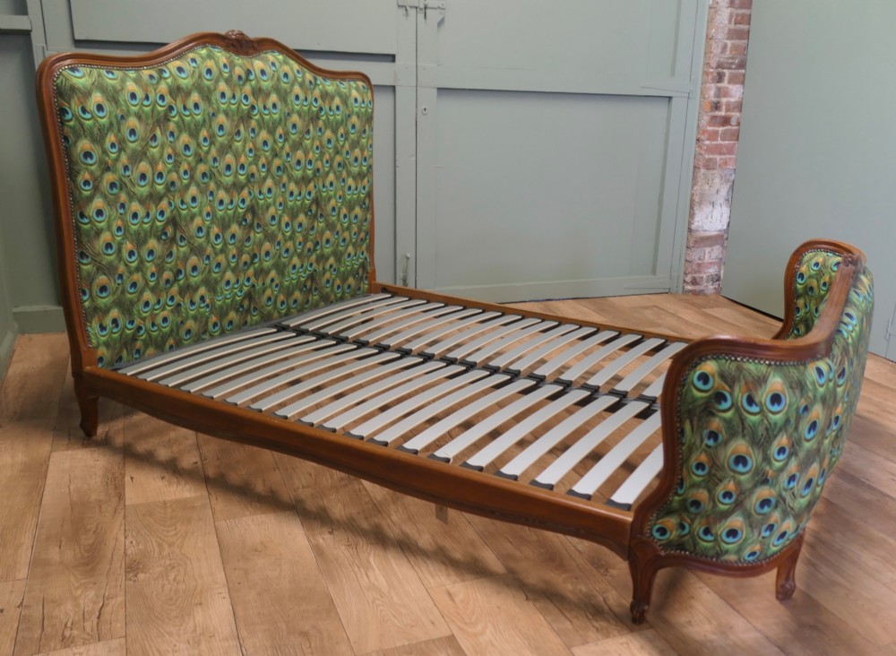 A French Louis XV style double bed frame featuring carved wooden borders, a padded headboard, and a curved corbeille footboard upholstered in green peacock feather patterned fabric with studding. View VI