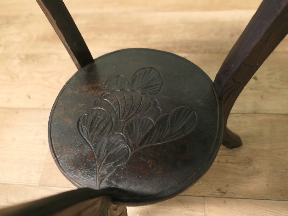 A dark oak circular Arts and Crafts lamp table featuring carved sunflower motifs around the rim, curved legs, and a lower circular tier. View V