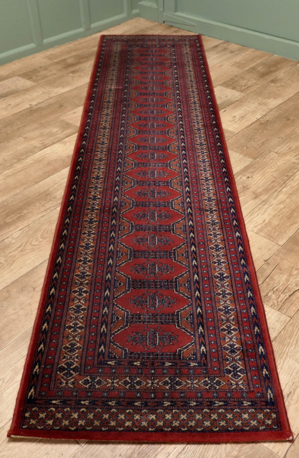 A long wool hallway runner carpet with repeating red geometric hexagonal medallions surrounded by patterned navy blue and terracotta borders.