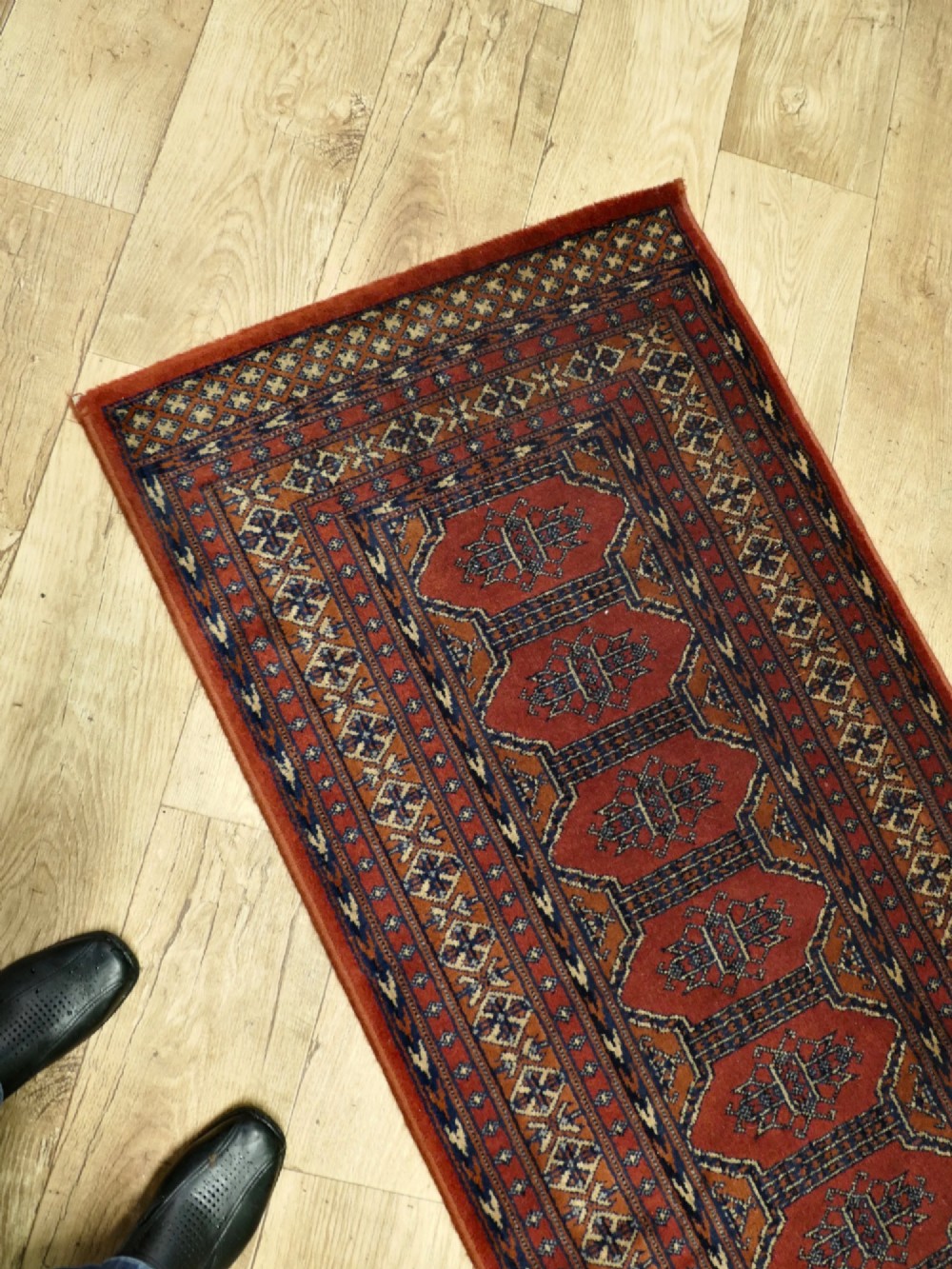 A long wool hallway runner carpet with repeating red geometric hexagonal medallions surrounded by patterned navy blue and terracotta borders. View VII