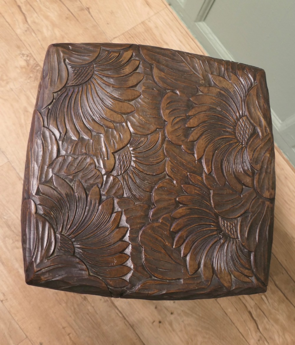 A square dark oak Arts and Crafts side table featuring hand-carved sunflower motifs across the top and lower shelf, supported by four gently curved legs. View V
