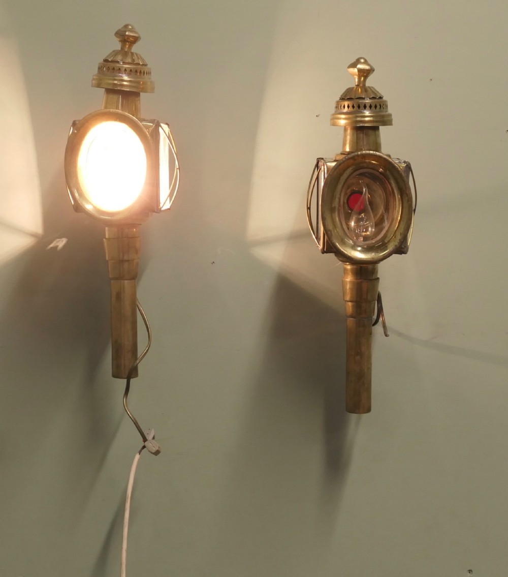 A pair of electrified brass French carriage lanterns mounted on a wall, featuring circular front glass lenses, top finials, and tubular shafts.