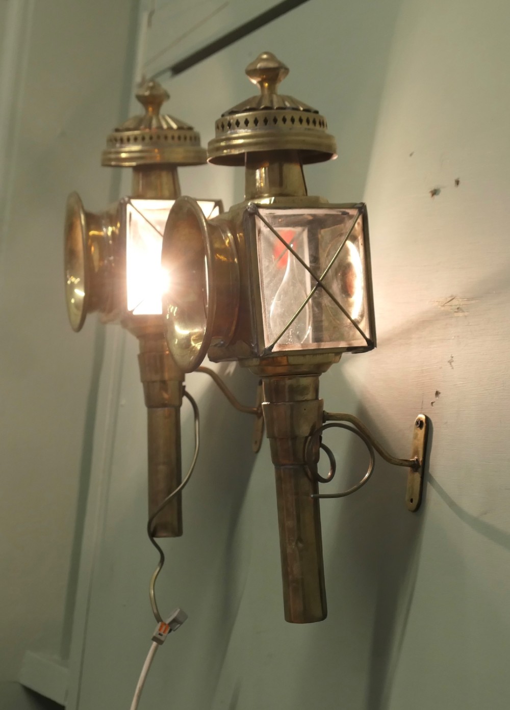 A pair of electrified brass French carriage lanterns mounted on a wall, featuring circular front glass lenses, top finials, and tubular shafts. View III