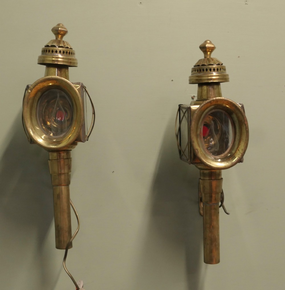 A pair of electrified brass French carriage lanterns mounted on a wall, featuring circular front glass lenses, top finials, and tubular shafts. View IV