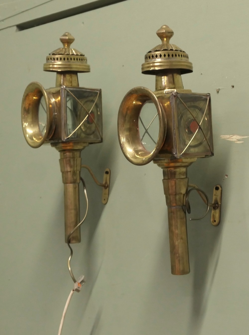 A pair of electrified brass French carriage lanterns mounted on a wall, featuring circular front glass lenses, top finials, and tubular shafts. View V