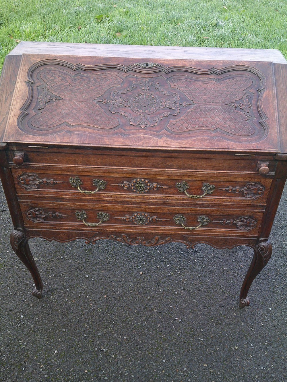 A French carved oak writing bureau featuring a sloping fall-front flap, two drawers with brass handles, and cabriole legs.