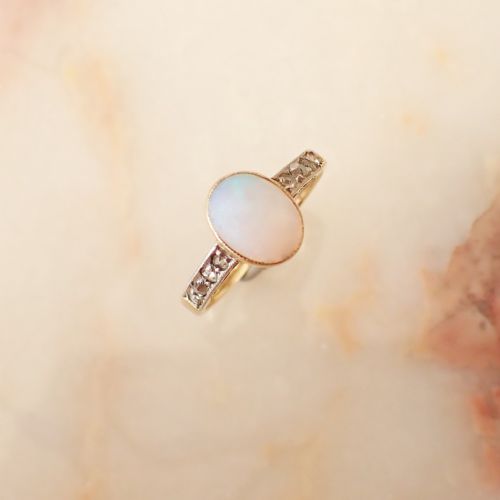 fig 1. An Edwardian 15ct yellow gold ring featuring an oval cabochon opal centre stone flanked by diamond-set decorative shoulders.