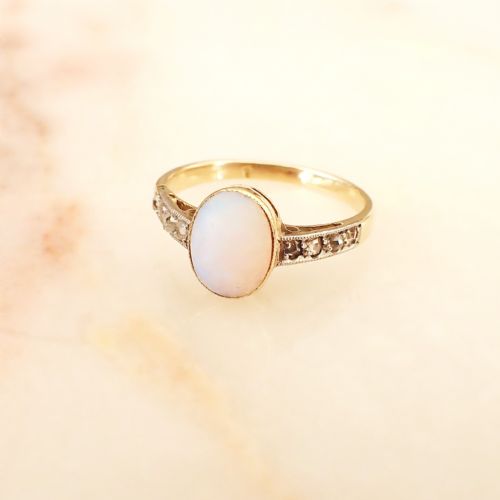 fig 2. An Edwardian 15ct yellow gold ring featuring an oval cabochon opal centre stone flanked by diamond-set decorative shoulders.