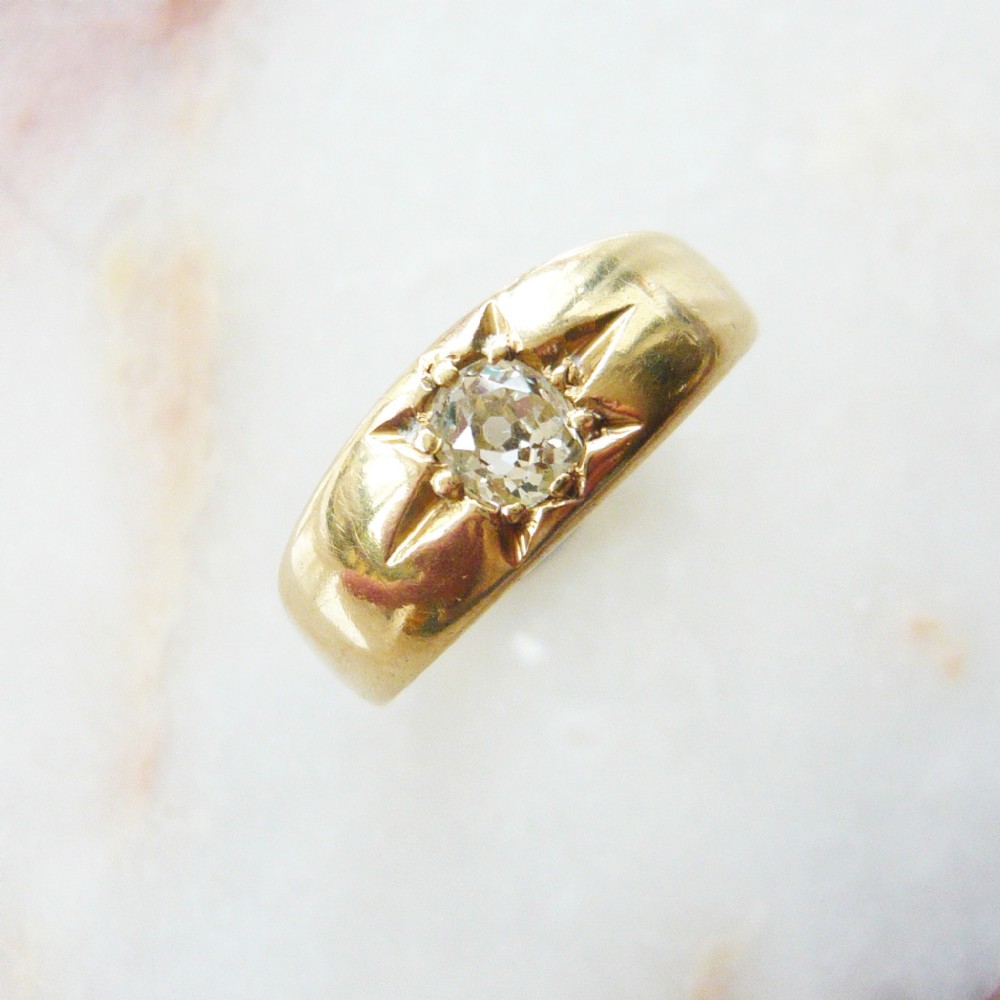 A Victorian yellow gold band ring featuring a single cushion cut diamond flush set inside an engraved starburst motif.