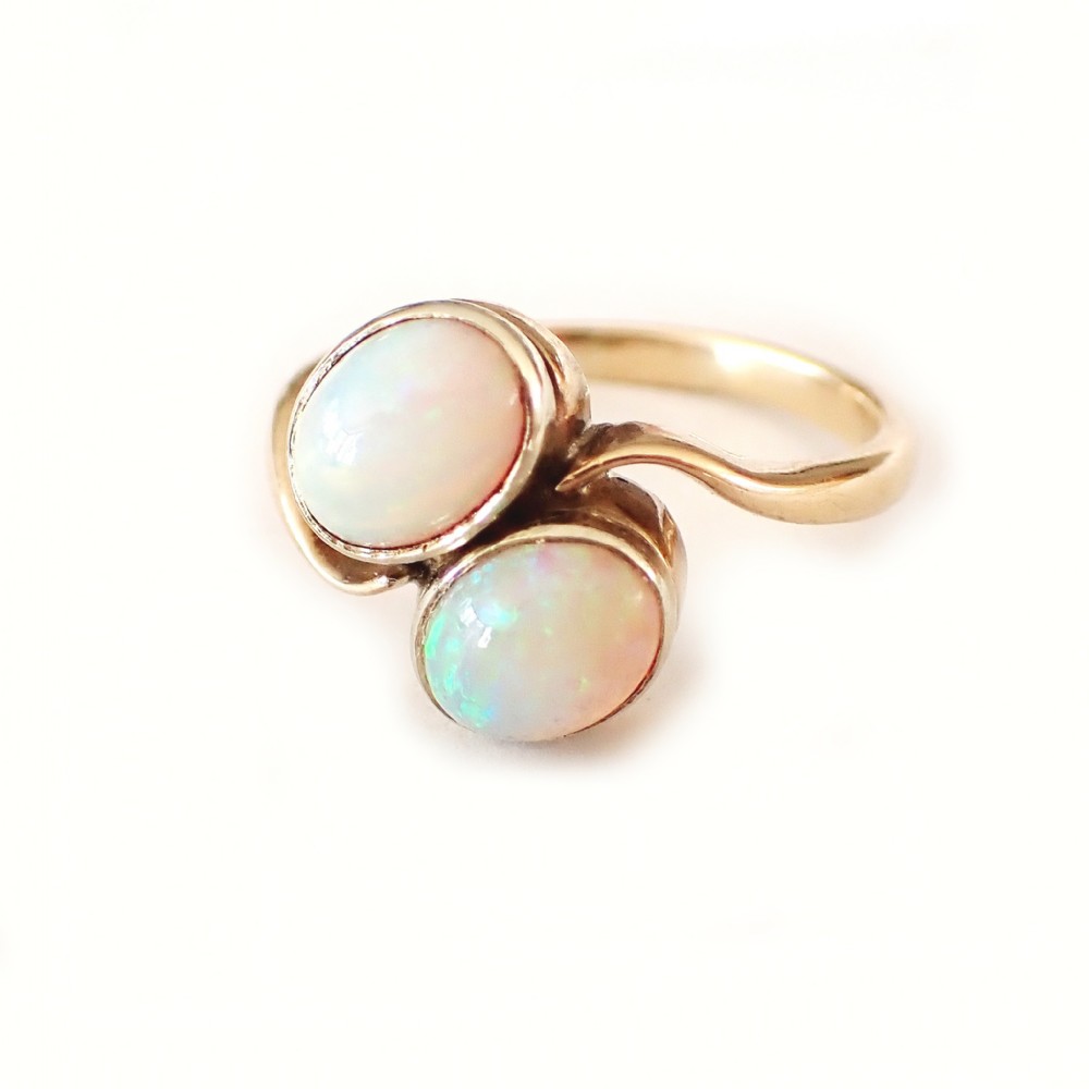 An Edwardian gold Toi et Moi ring featuring two oval cabochon opals set side by side on a fluid bypass band.