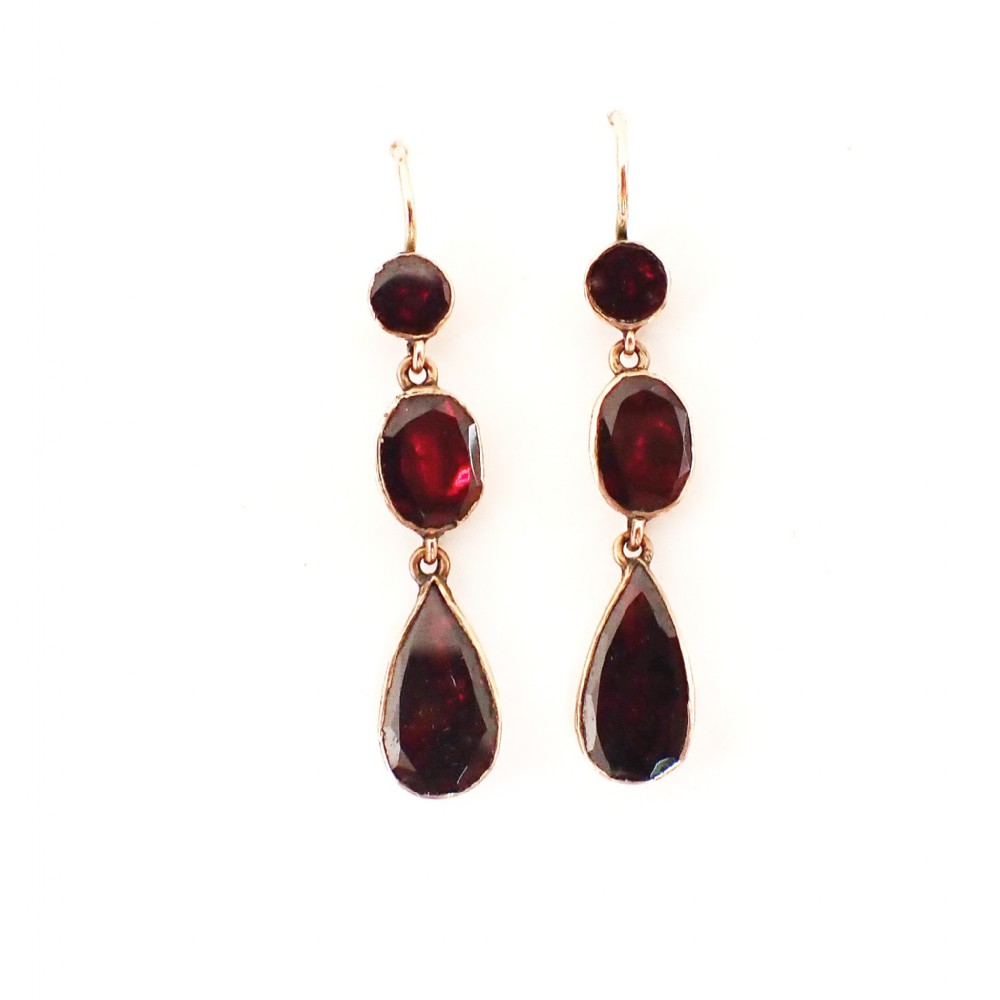 A pair of antique gold drop earrings featuring three articulated faceted deep red garnets in round, oval, and pear shapes.