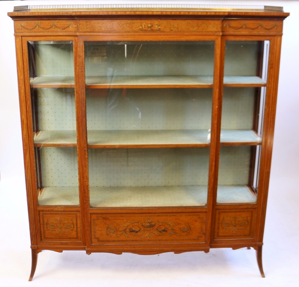 An Edwardian satinwood display cabinet featuring a breakfront design with glazed panels, floral marquetry inlay, and a brass top gallery.