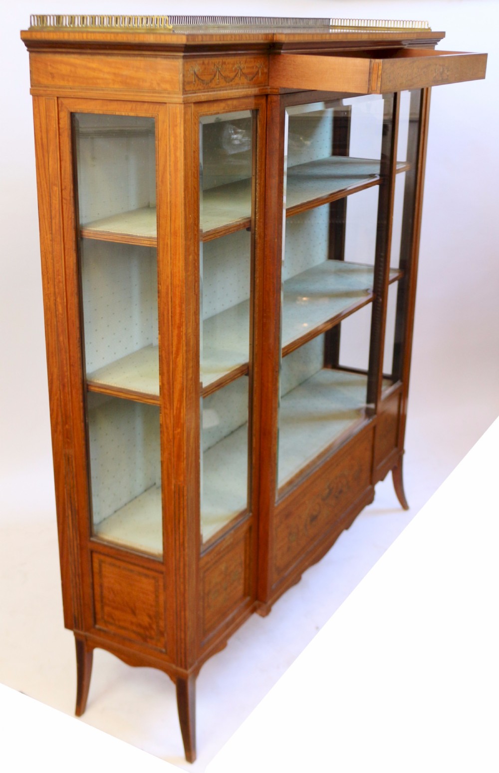 An Edwardian satinwood display cabinet featuring a breakfront design with glazed panels, floral marquetry inlay, and a brass top gallery. View II