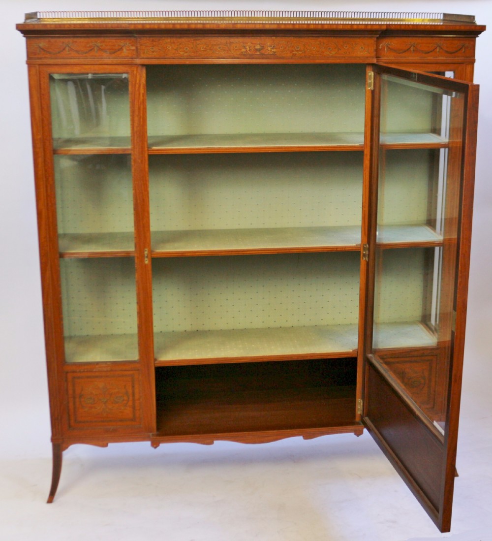 An Edwardian satinwood display cabinet featuring a breakfront design with glazed panels, floral marquetry inlay, and a brass top gallery. View V