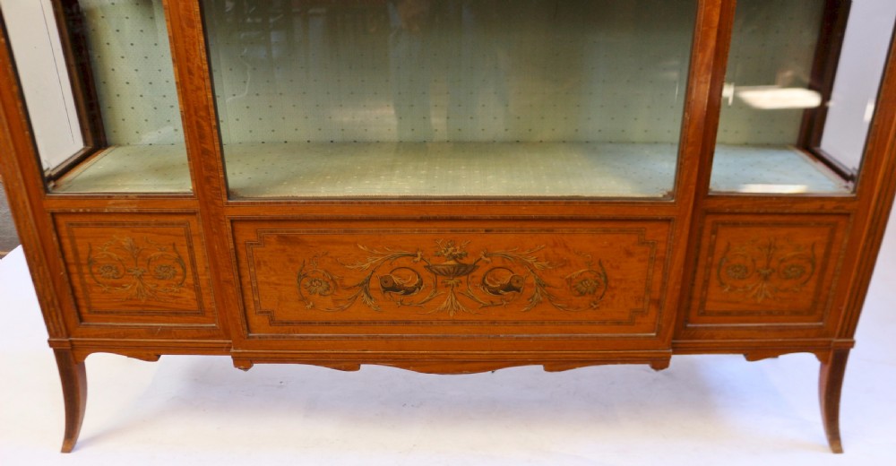 An Edwardian satinwood display cabinet featuring a breakfront design with glazed panels, floral marquetry inlay, and a brass top gallery. View VII
