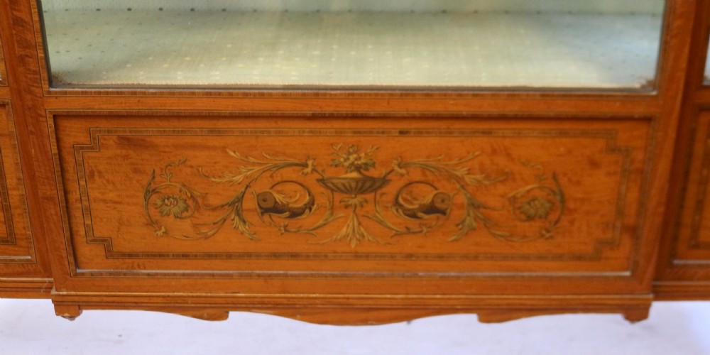 An Edwardian satinwood display cabinet featuring a breakfront design with glazed panels, floral marquetry inlay, and a brass top gallery. View VIII