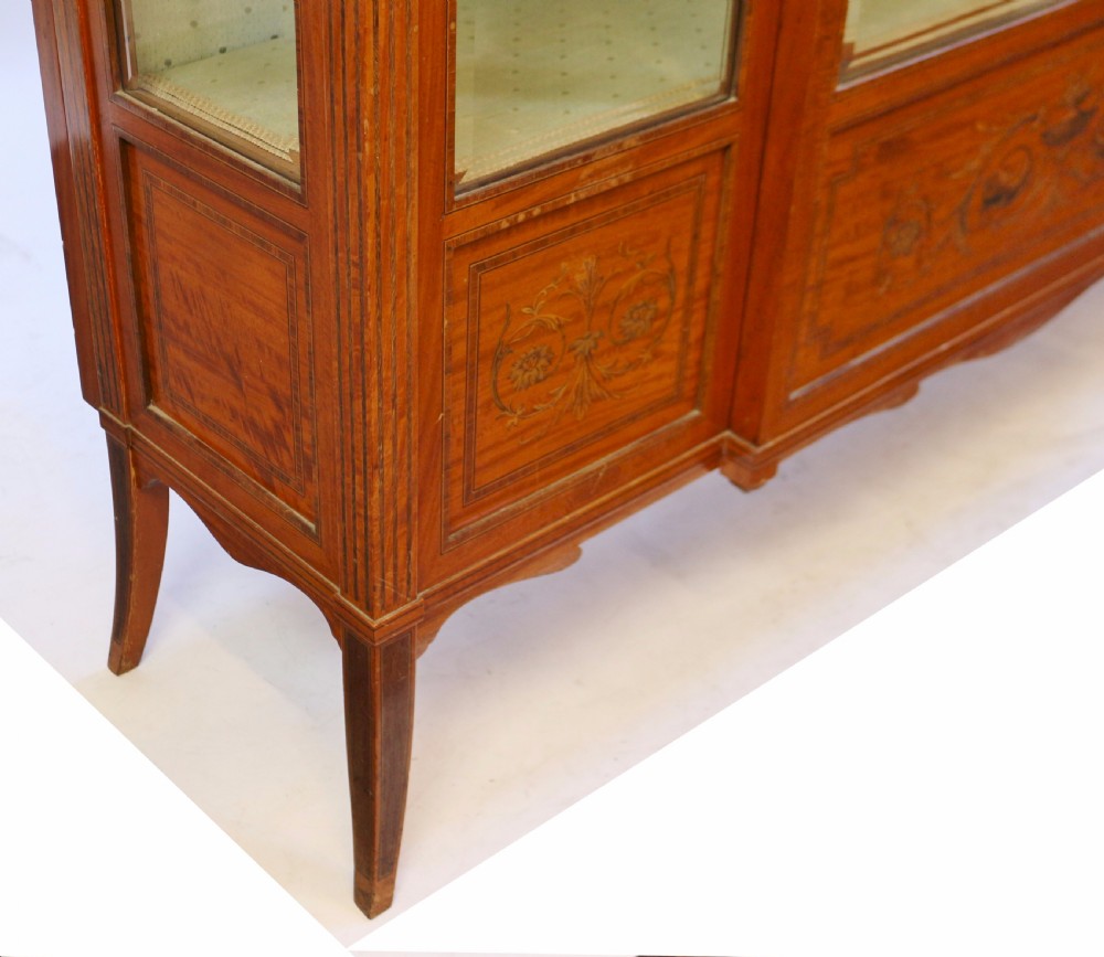 An Edwardian satinwood display cabinet featuring a breakfront design with glazed panels, floral marquetry inlay, and a brass top gallery. View IX