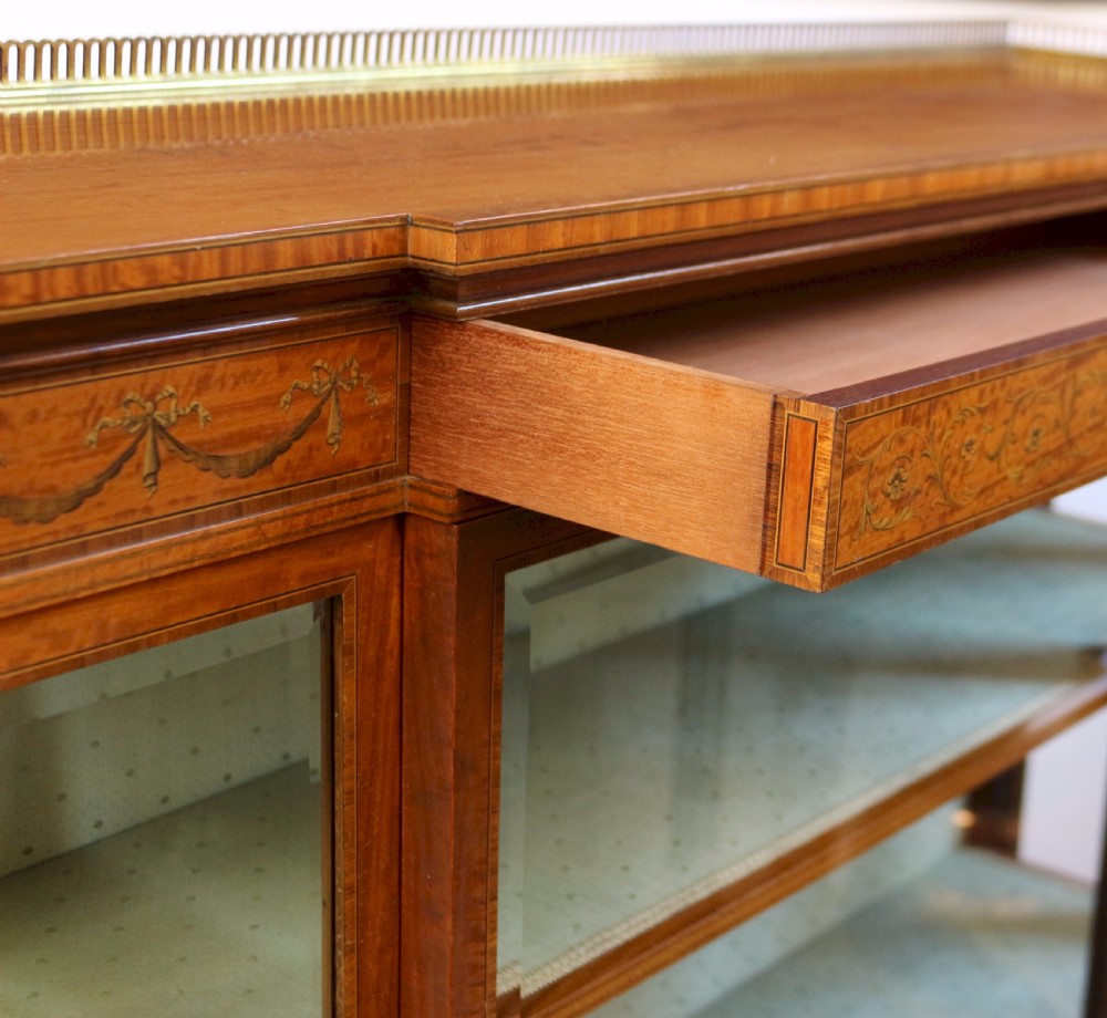 An Edwardian satinwood display cabinet featuring a breakfront design with glazed panels, floral marquetry inlay, and a brass top gallery. View XII