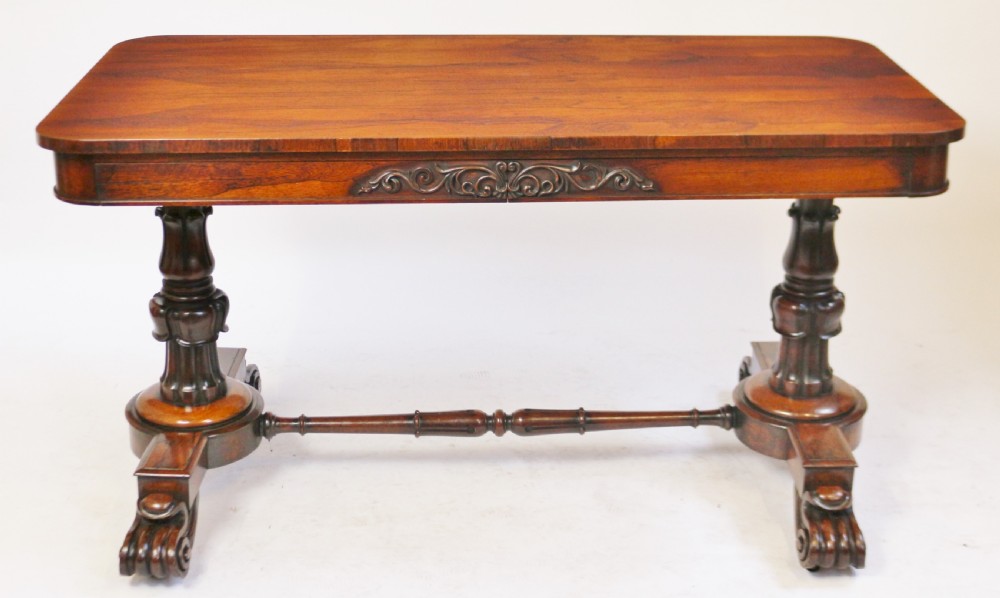 A William IV rosewood centre table featuring a rectangular top with rounded corners, a carved frieze, turned end supports, a low stretcher, and scroll feet.