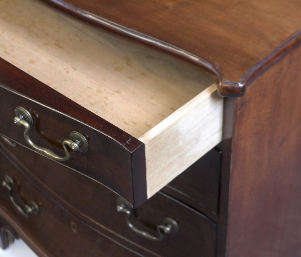 A George III mahogany serpentine chest of drawers featuring four drawers with brass swan-neck handles and bracket feet. View V