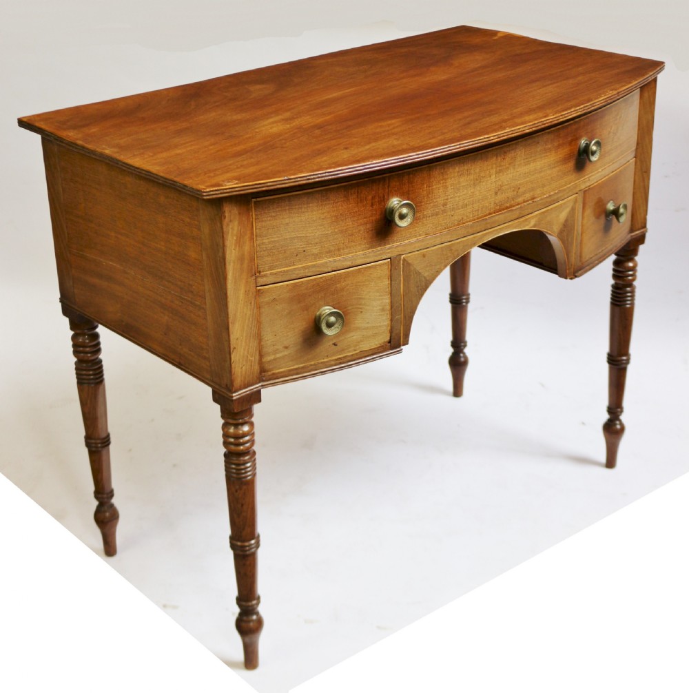 A Regency mahogany bowfront side table featuring three drawers with brass knob handles, an arched kneehole centre, and four turned legs. View II