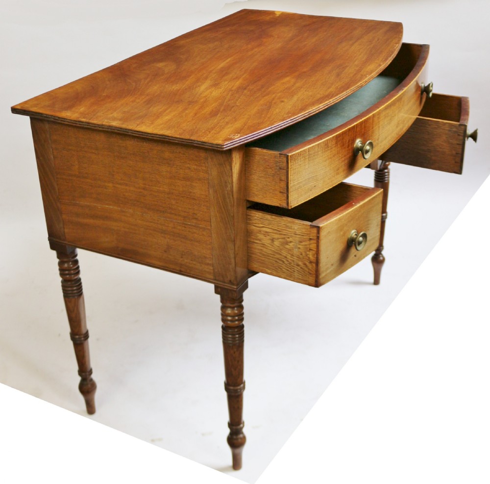 A Regency mahogany bowfront side table featuring three drawers with brass knob handles, an arched kneehole centre, and four turned legs. View III