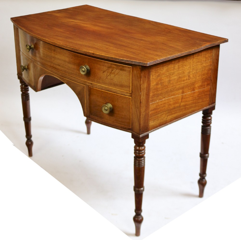 A Regency mahogany bowfront side table featuring three drawers with brass knob handles, an arched kneehole centre, and four turned legs. View IV