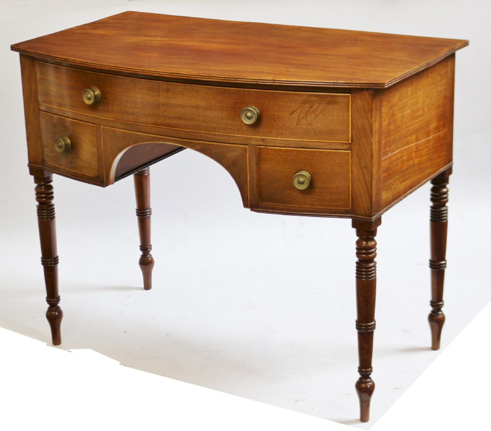 A Regency mahogany bowfront side table featuring three drawers with brass knob handles, an arched kneehole centre, and four turned legs. View V
