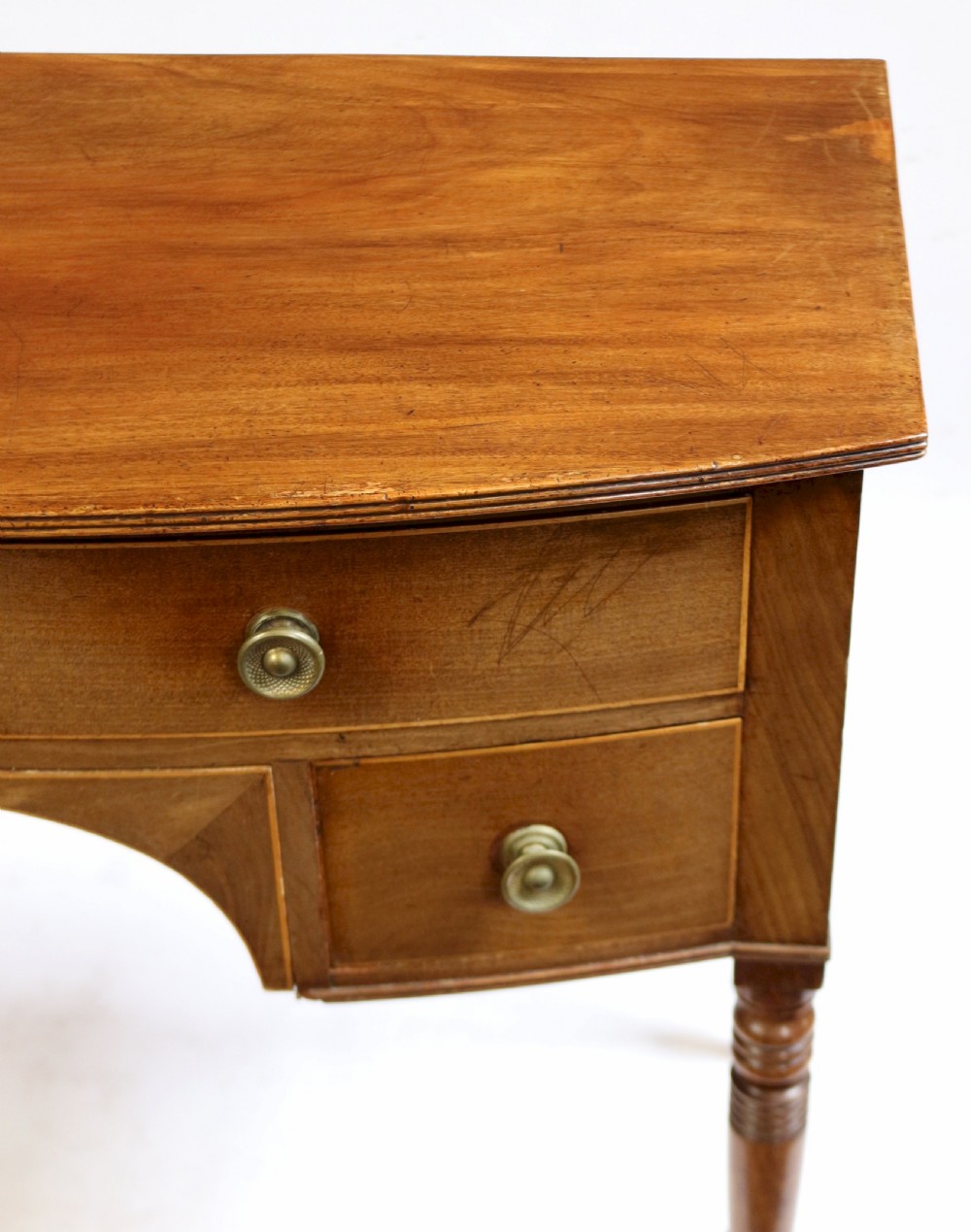 A Regency mahogany bowfront side table featuring three drawers with brass knob handles, an arched kneehole centre, and four turned legs. View VII