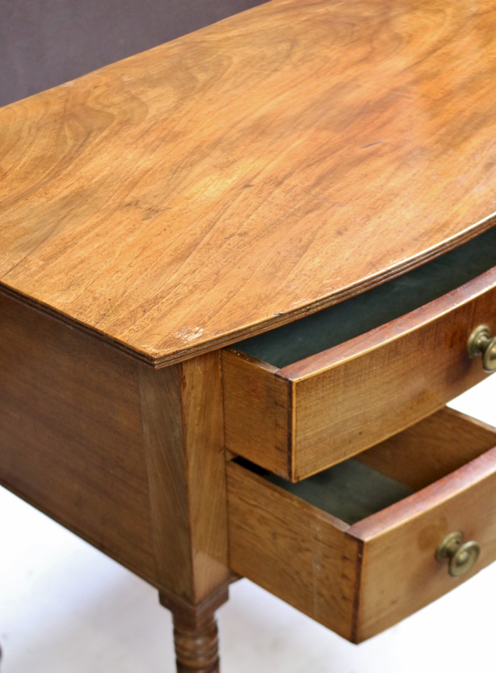A Regency mahogany bowfront side table featuring three drawers with brass knob handles, an arched kneehole centre, and four turned legs. View VIII