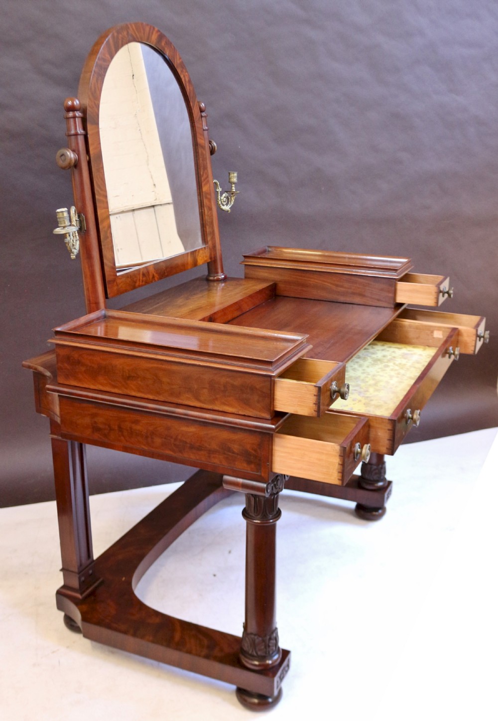 A William IV mahogany dressing table featuring an arched swivel mirror, brass sconces, upper drawers, and carved front columns on a plinth base. View II