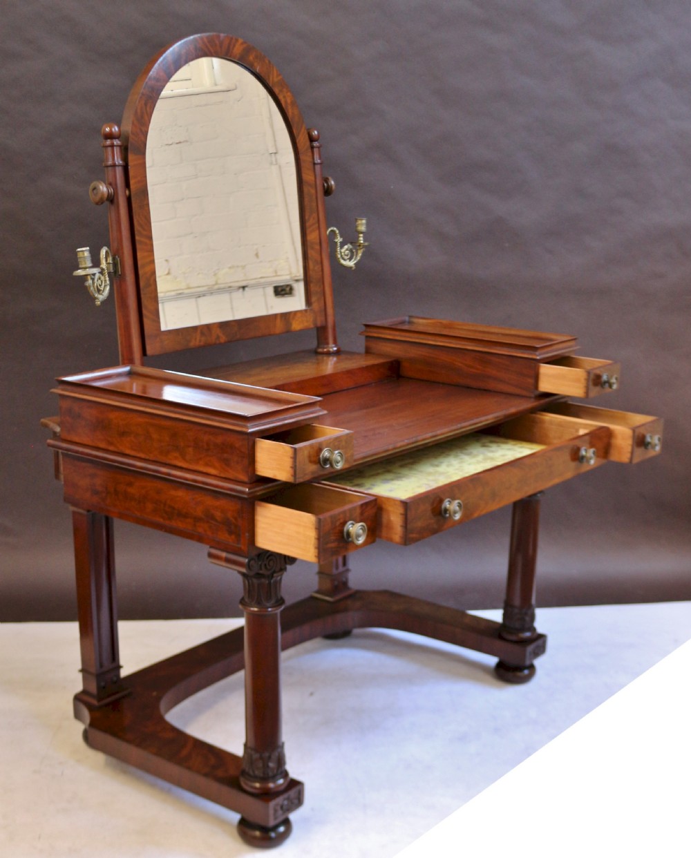 A William IV mahogany dressing table featuring an arched swivel mirror, brass sconces, upper drawers, and carved front columns on a plinth base. View III