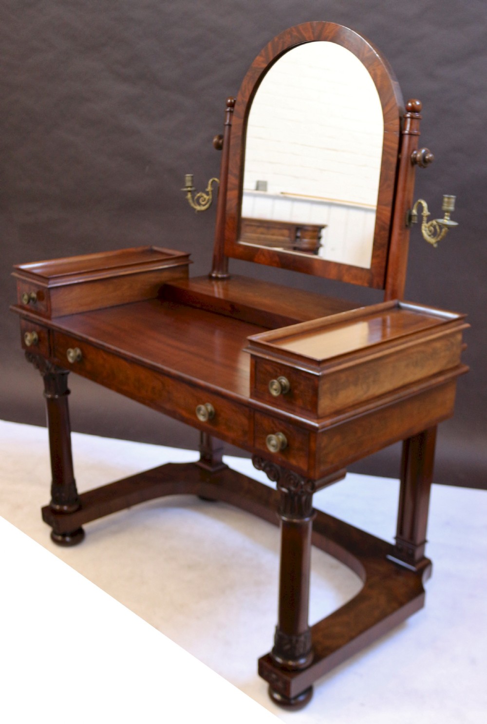 A William IV mahogany dressing table featuring an arched swivel mirror, brass sconces, upper drawers, and carved front columns on a plinth base. View IV