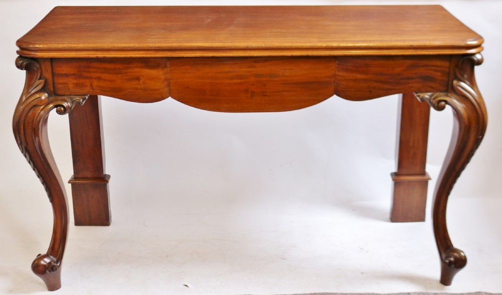 A Victorian mahogany console table featuring carved cabriole front legs with scroll feet, a shaped front apron, and a flat polished surface.