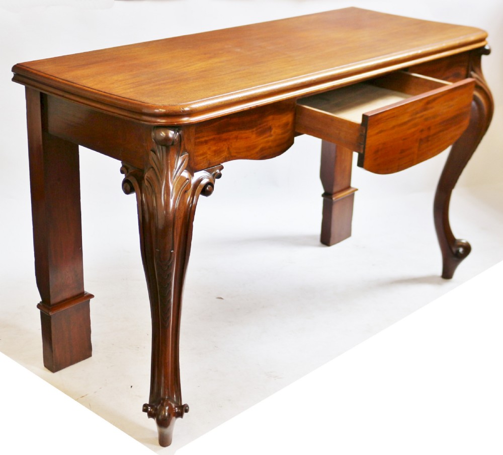 A Victorian mahogany console table featuring carved cabriole front legs with scroll feet, a shaped front apron, and a flat polished surface. View IV