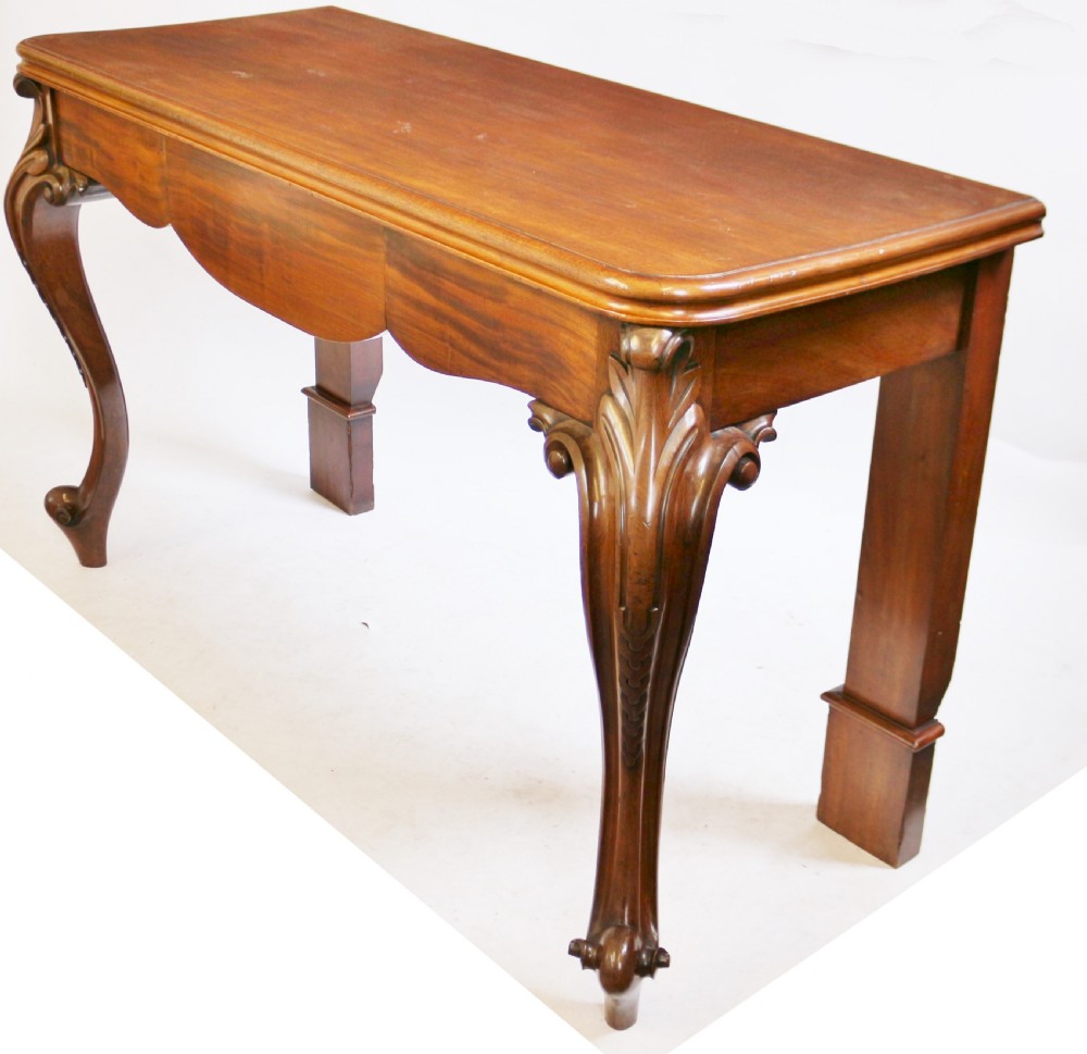 A Victorian mahogany console table featuring carved cabriole front legs with scroll feet, a shaped front apron, and a flat polished surface. View V