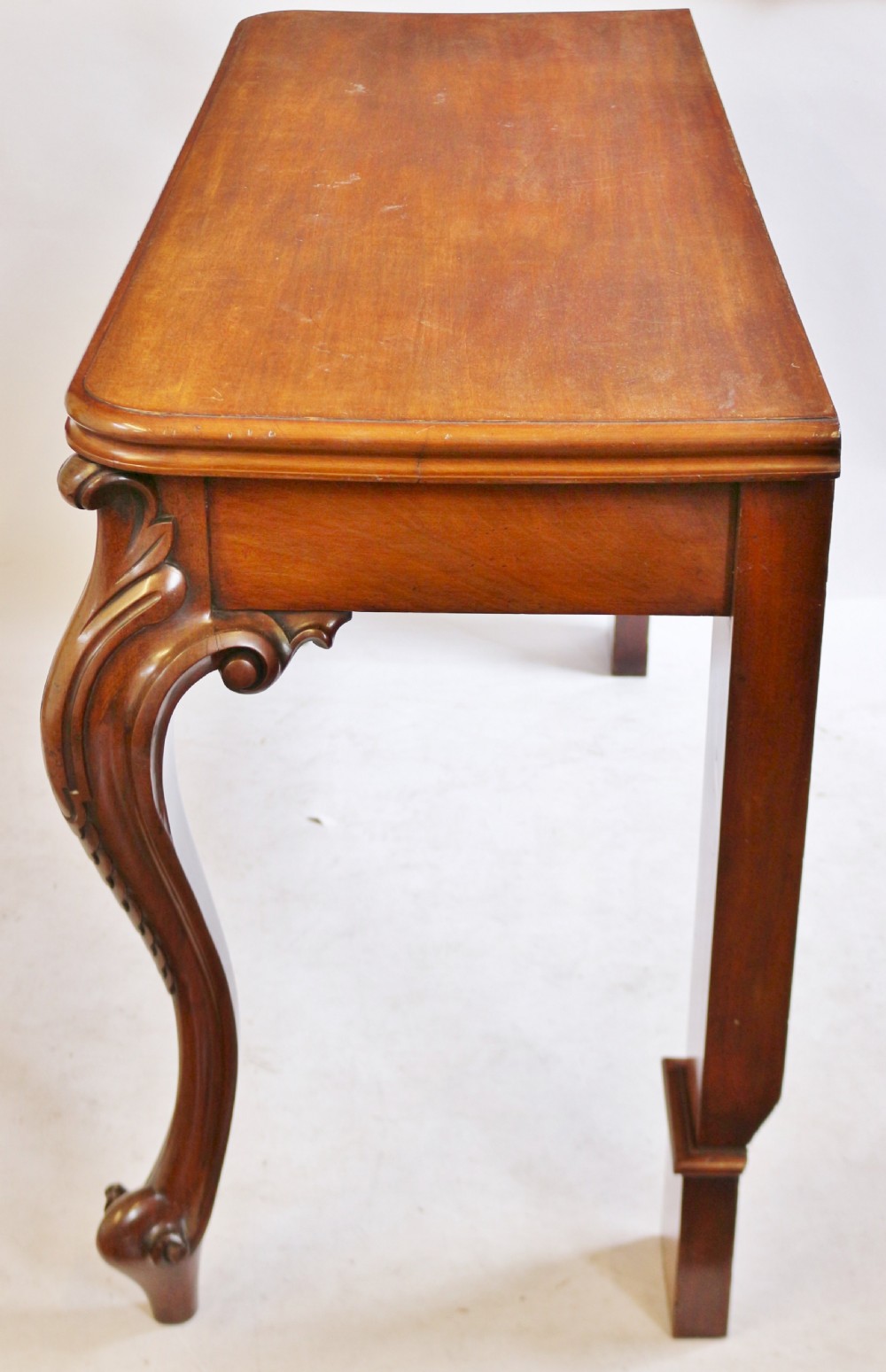 A Victorian mahogany console table featuring carved cabriole front legs with scroll feet, a shaped front apron, and a flat polished surface. View VI