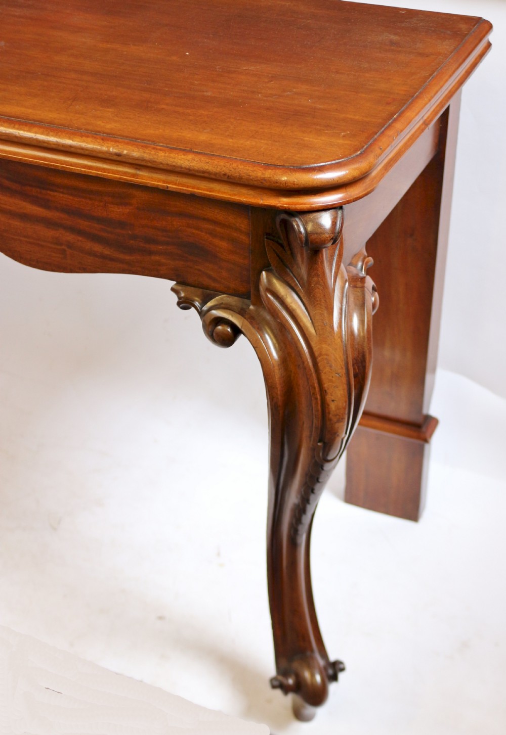 A Victorian mahogany console table featuring carved cabriole front legs with scroll feet, a shaped front apron, and a flat polished surface. View VII