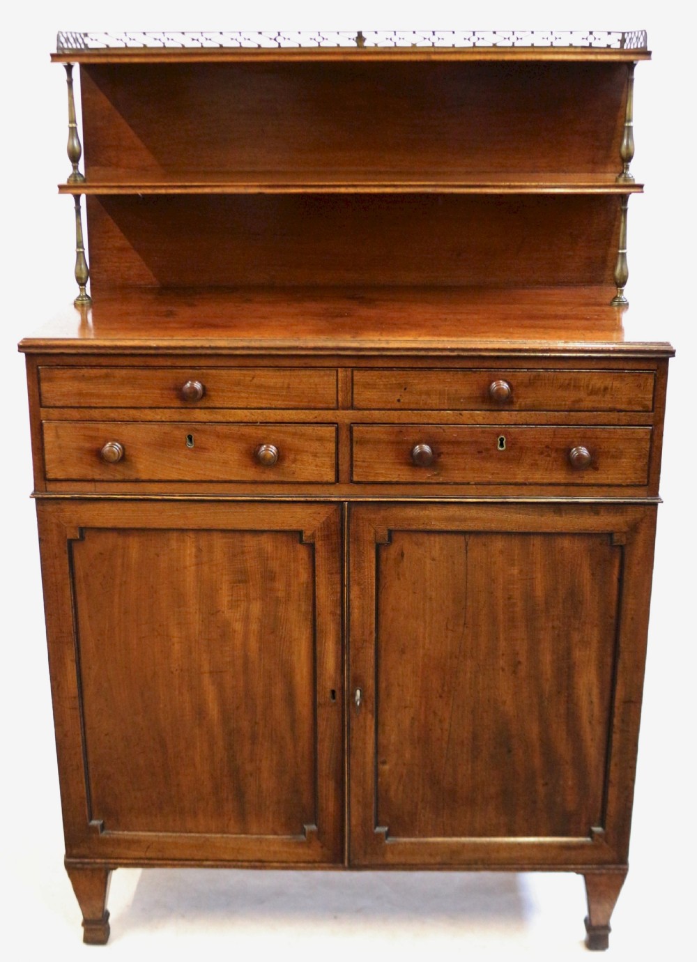 A Regency mahogany chiffonier with a two-tier brass-galleried shelf unit above a fitted writing drawer and two-door cabinet base.