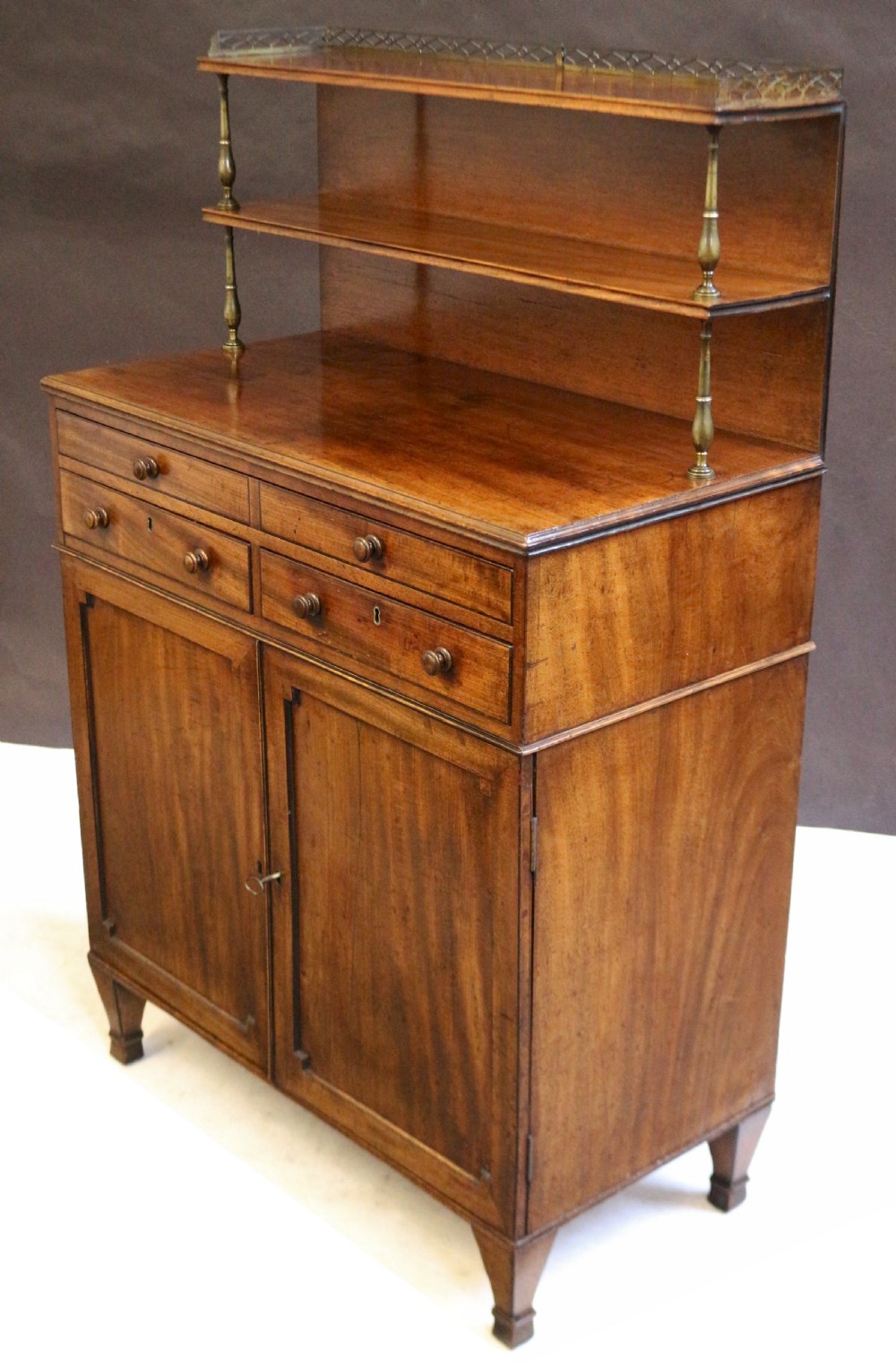 A Regency mahogany chiffonier with a two-tier brass-galleried shelf unit above a fitted writing drawer and two-door cabinet base. View X