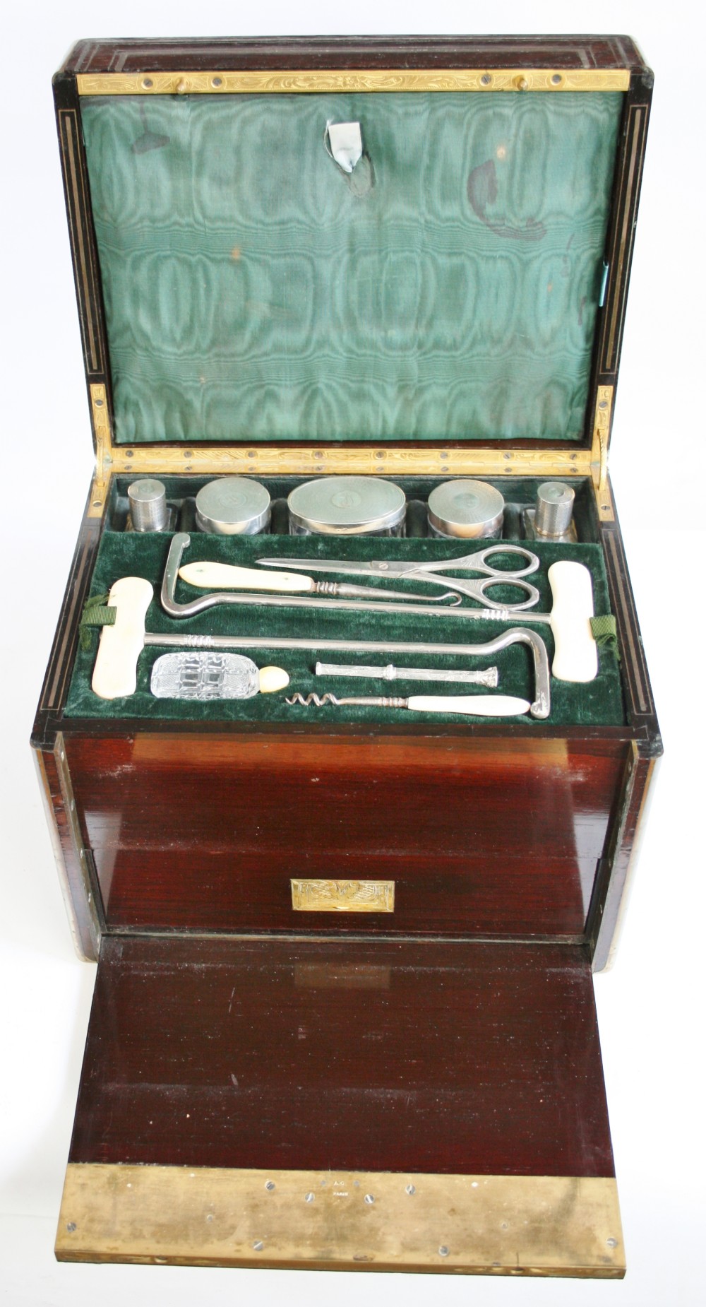 An opened 19th-century rosewood box with brass inlay featuring a green velvet fitted interior containing silver-capped jars and grooming implements.