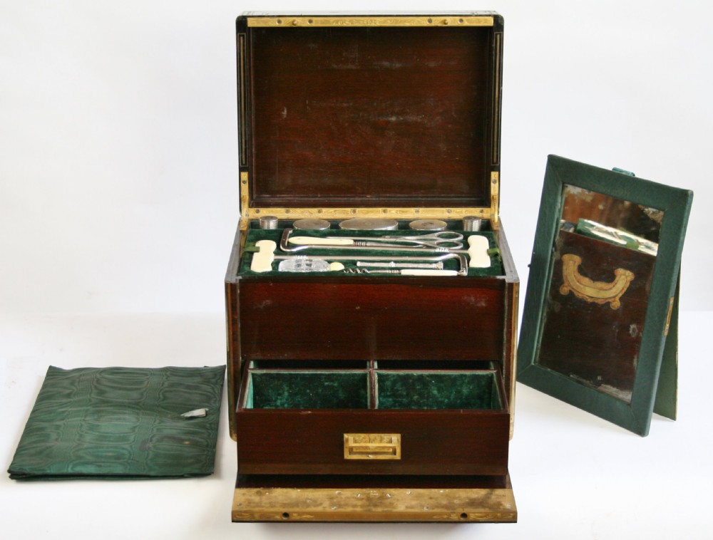 An opened 19th-century rosewood box with brass inlay featuring a green velvet fitted interior containing silver-capped jars and grooming implements. View X