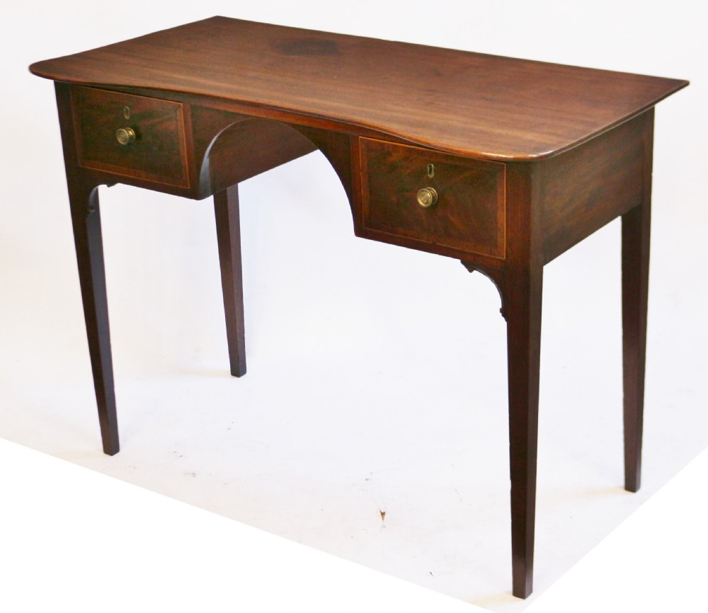 A George III mahogany kneehole table featuring a gently curved front, two string-inlaid drawers with brass handles, an arched central apron, and four square tapered legs. View II