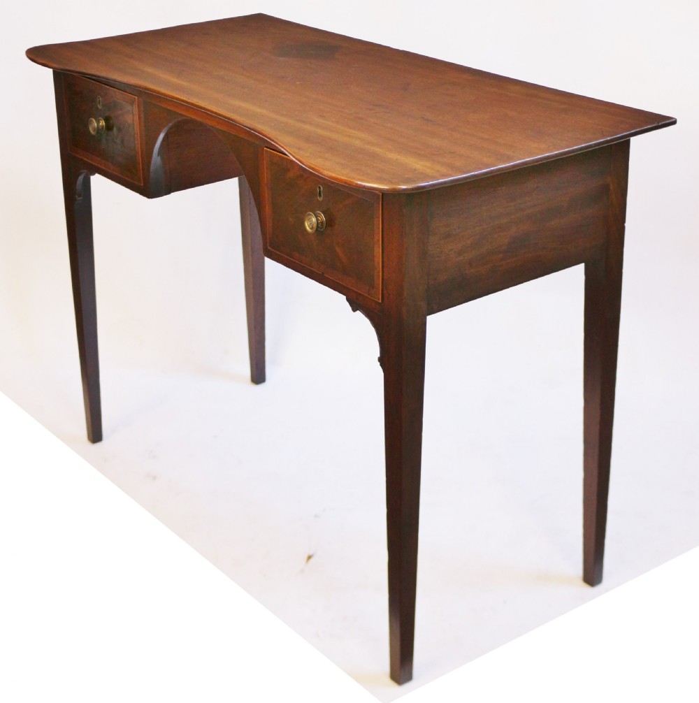 A George III mahogany kneehole table featuring a gently curved front, two string-inlaid drawers with brass handles, an arched central apron, and four square tapered legs. View III
