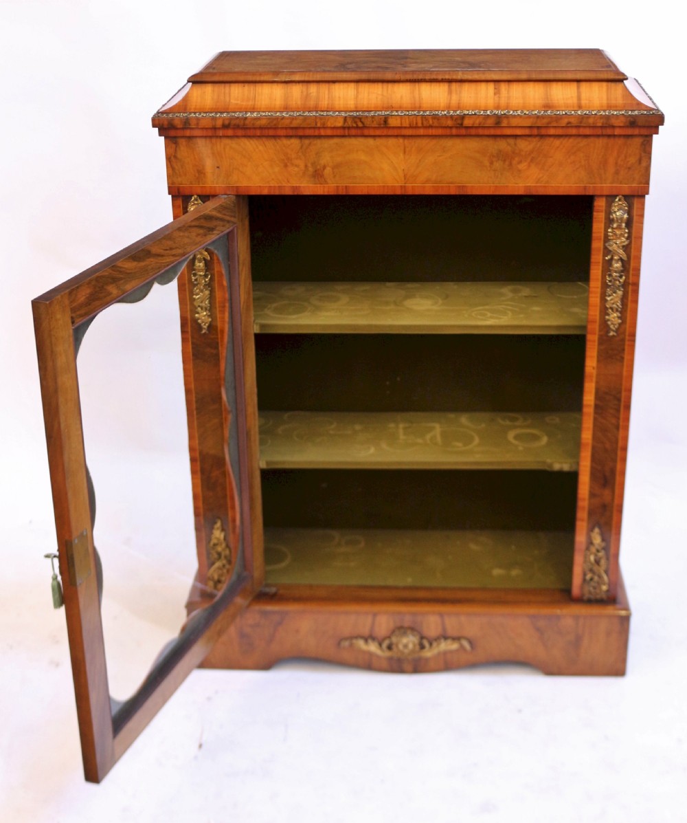 A Victorian walnut and kingwood pier cabinet with a single glazed door, brass mounts, and internal display shelves. View VI