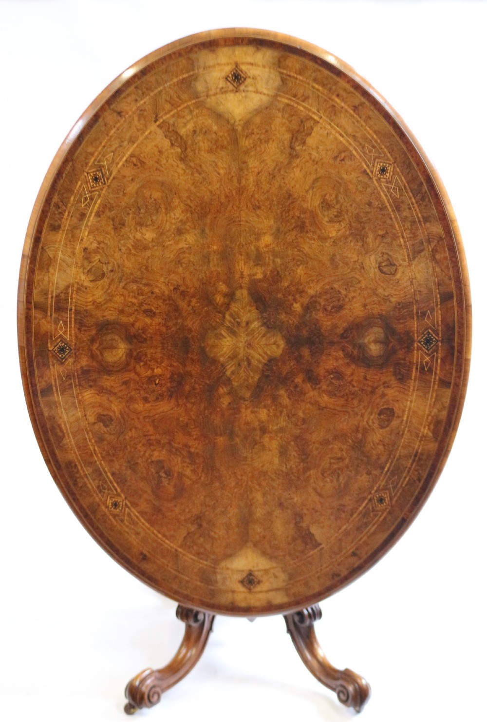 An antique Victorian oval tilt-top loo table crafted from figured walnut with marquetry inlay and carved pedestal legs.