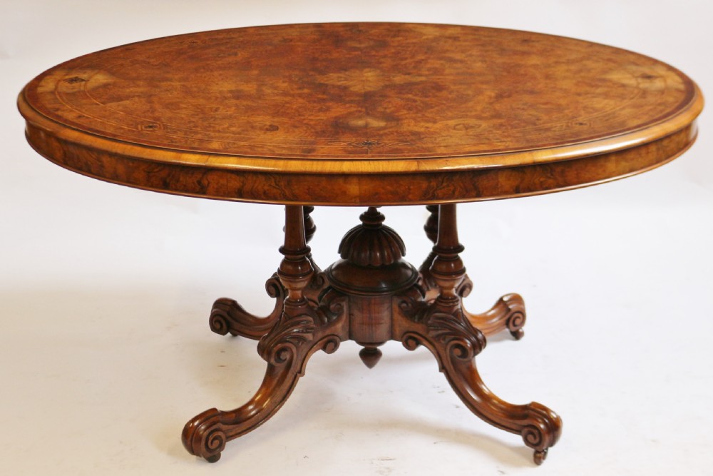An antique Victorian oval tilt-top loo table crafted from figured walnut with marquetry inlay and carved pedestal legs. View II
