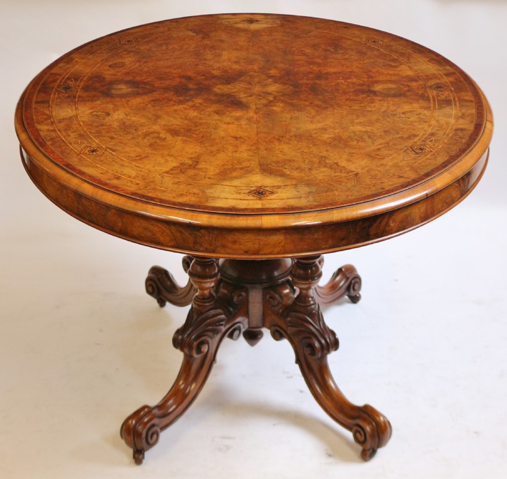 An antique Victorian oval tilt-top loo table crafted from figured walnut with marquetry inlay and carved pedestal legs. View IV