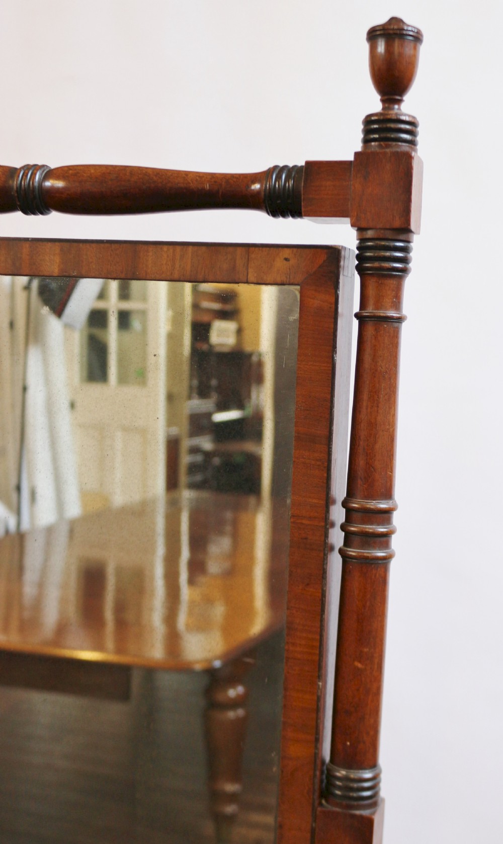 A Regency mahogany cheval mirror featuring a rectangular swivelling frame set between turned upright posts with brass castors. View VI